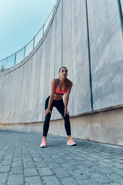 Piena lunghezza di stanca giovane donna in abbigliamento sportivo in piedi all'aperto — Foto Stock