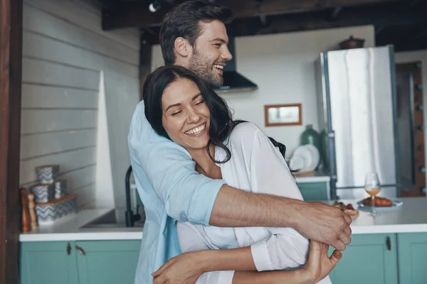 Kochająca młoda para uśmiecha się i przytula podczas spędzania czasu w kuchni — Zdjęcie stockowe