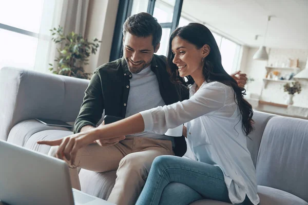 Bella coppia giovane bere caffè e guardando sul computer portatile mentre seduto sul divano a casa — Foto Stock