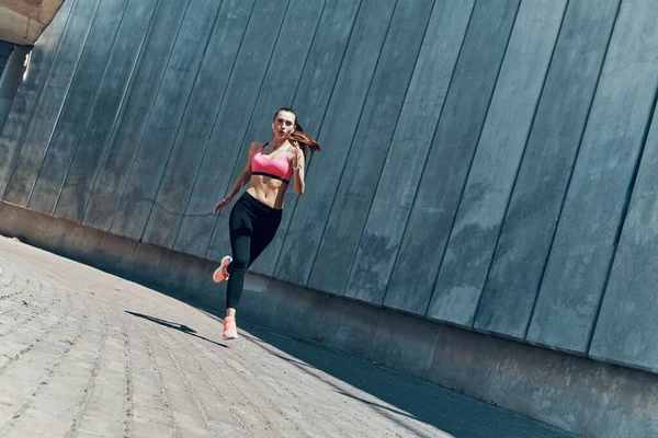Comprimento total de bela jovem mulher em roupas esportivas correndo ao ar livre — Fotografia de Stock