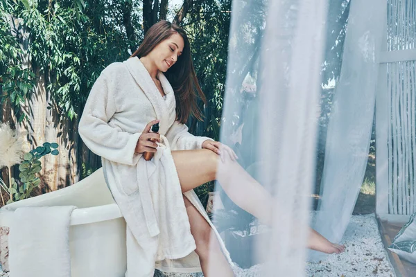 Приваблива молода усміхнена жінка зволожує крем, спираючись на ванну на відкритому повітрі — стокове фото