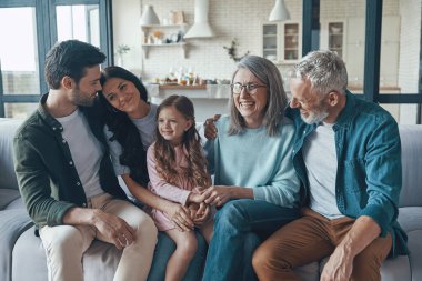 Mutlu bir aile birlikte vakit geçirir ve evdeki kanepede otururken gülümser.