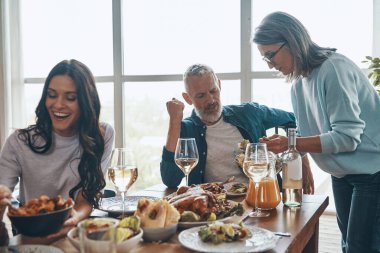 Mutlu çok nesilli aile, modern dairede otururken yemeğin tadını çıkarıyor ve gülümsüyor.