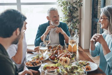 Gülümseyen çok nesildir aile, modern dairede otururken lezzetli bir akşam yemeğinin tadını çıkarıyor.