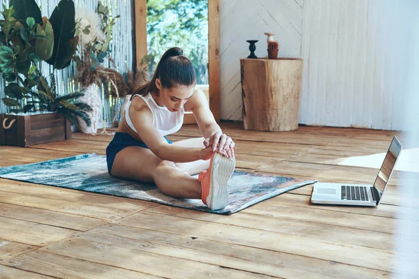 Bella giovane donna in abbigliamento sportivo che si estende sul patio con il computer portatile posa vicino a lei — Foto Stock