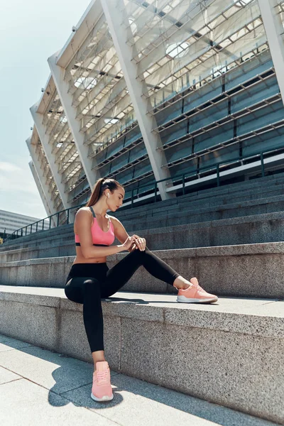 Attraente giovane donna in abbigliamento sportivo controllare il suo orologio intelligente mentre seduto all'aperto — Foto Stock