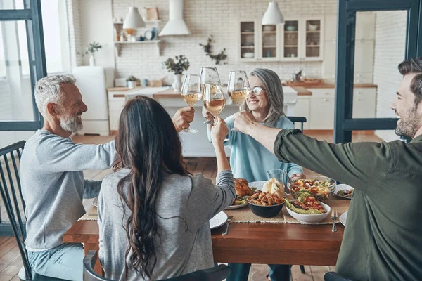 Bonne famille multi-génération trinquant l'un l'autre et souriant tout en dînant ensemble — Photo