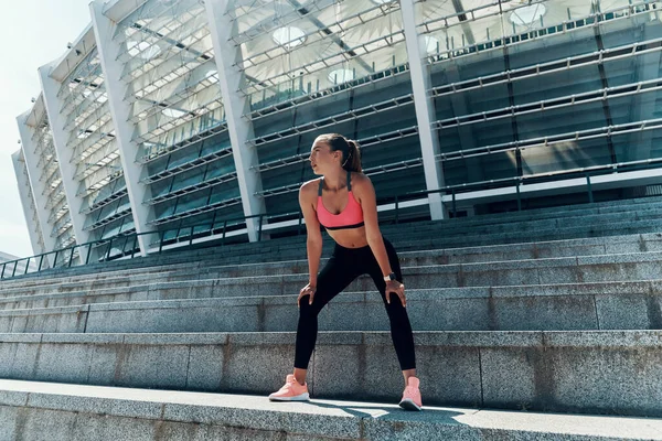 Piena lunghezza di fiduciosa giovane donna in abbigliamento sportivo guardando altrove mentre in piedi all'aperto — Foto Stock