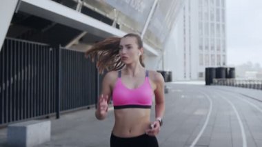 Spor elbiseli, kendinden emin genç bir kadın açık havada koşuyor.