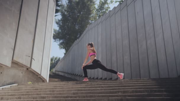 Självsäker ung kvinna i sportkläder gör stretching övningar utomhus — Stockvideo