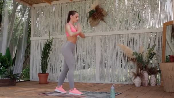 Side view of beautiful young woman in sports clothing exercising on patio — Stock Video