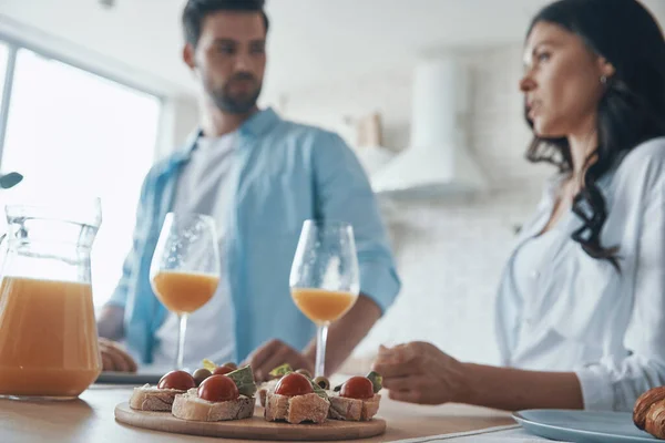 Gyönyörű fiatal pár beszél és készít reggelit, miközben időt tölt a hazai konyhában — Stock Fotó