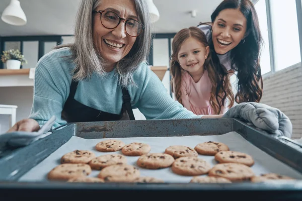 Heureuse femme âgée sortant les biscuits du four et souriant tout en passant du temps en famille — Photo