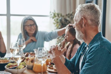 Mutlu çoklu nesil aile yemeği yerken iletişim kuruyor ve gülümsüyor.