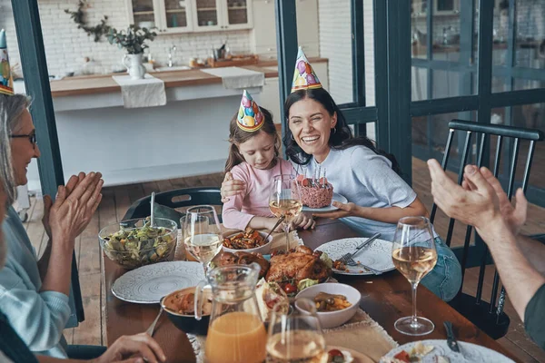 Feliz familia celebrando el cumpleaños de la niña mientras está sentada en la mesa del comedor en casa —  Fotos de Stock