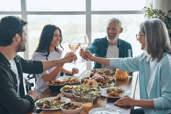 Mutlu çoklu kuşak aile kadeh kaldırıyor ve birlikte yemek yerken gülümsüyor.