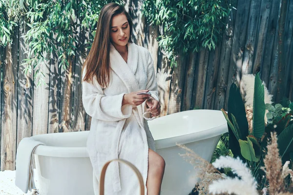 Belle jeune femme crème hydratante pour les mains tout en se penchant à la baignoire à l'extérieur — Photo