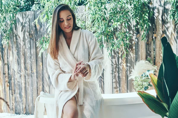 Hermosa mujer joven crema hidratante para las manos mientras se inclina en la bañera al aire libre —  Fotos de Stock