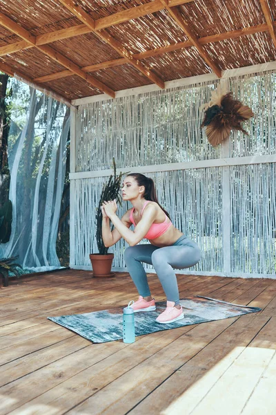 Piękna młoda kobieta w sportowej odzieży squatting na patio — Zdjęcie stockowe