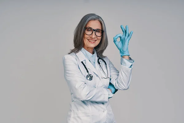 Starší krásná žena lékař dávat na chirurgické rukavice a usmívat — Stock fotografie