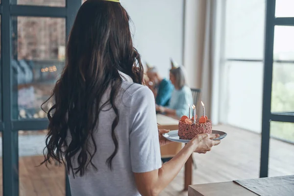 Rückansicht einer Frau mit Geburtstagstorte, während Gäste im Wohnzimmer warten — Stockfoto