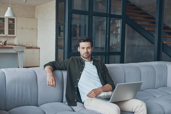 Knappe jongeman met laptop terwijl hij thuis op de bank zit — Stockfoto