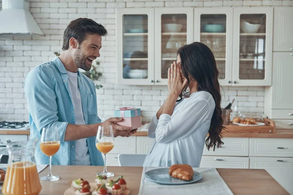 Joven dando una caja de regalo a su novia mientras desayuna en la cocina doméstica — Foto de Stock