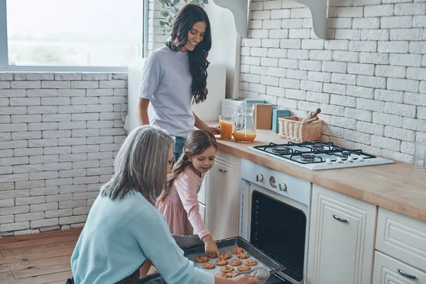 Beautiful grandmother taking out cookies from the oven and smiling while spending time with family — Stock fotografie