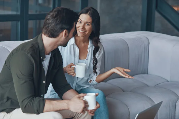 Gyönyörű fiatal pár kávézik és kommunikál, miközben otthon ülnek a kanapén. — Stock Fotó