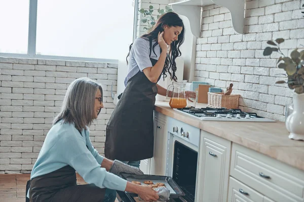 Красива молода жінка і її мати готують разом, проводячи час на домашній кухні — стокове фото