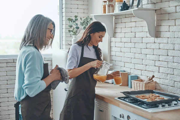 Bella giovane donna e sua madre che cucinano insieme mentre trascorrono del tempo in cucina domestica — Foto Stock
