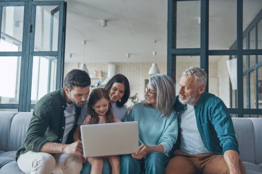 Mutlu aile dizüstü bilgisayar kullanıyor ve evde birlikte vakit geçirirken gülümsüyor.