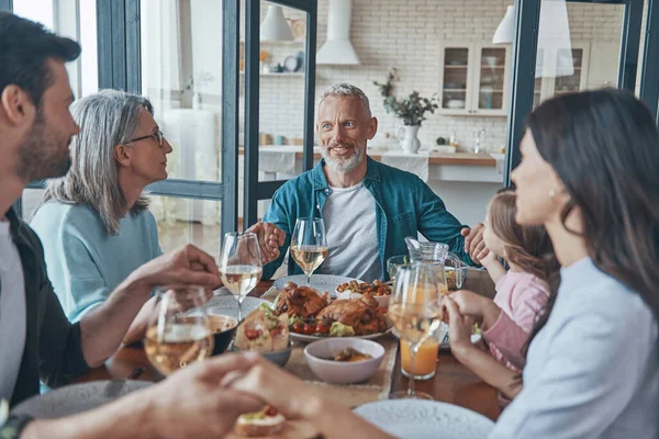 Happy multi-generation family holding hands and praying while having dinner together — Fotografia de Stock