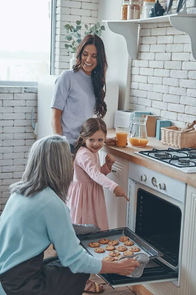 Beautiful grandmother taking out cookies from the oven and smiling while spending time with family — Stock fotografie