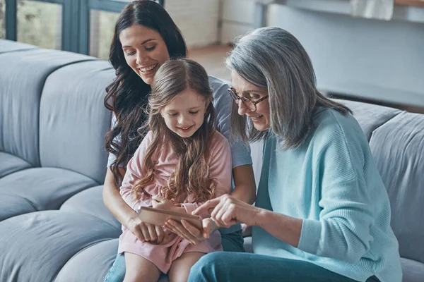 Happy little girl examining smart phone while spending time with mother and grandmother at home — Stock fotografie