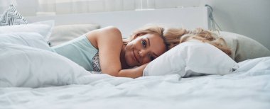 Çekici, gülümseyen bir kadın uyanıyor ve yatakta yatarken kameraya bakıyor.