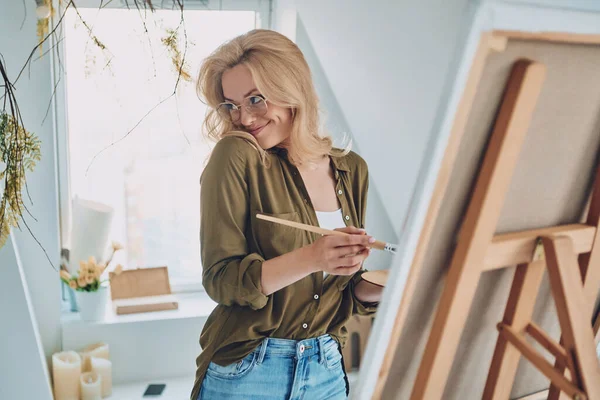 Atractivo joven cabello rubio mujer pintura en el estudio de arte y sonriendo —  Fotos de Stock