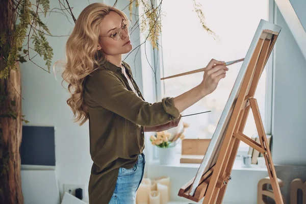 Zijaanzicht van aantrekkelijke jonge vrouw schilderen in kunststudio — Stockfoto