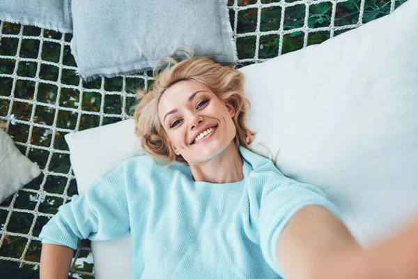 Top pohled na krásné mladé usmívající se žena dělat selfie při relaxaci ve velké houpací síti — Stock fotografie