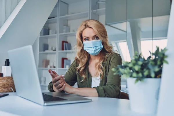 Attractive young woman in protective face mask sitting at the desk in office — Stock Photo, Image