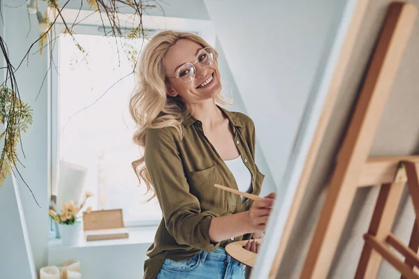 Atractivo joven cabello rubio mujer pintura en el estudio de arte y sonriendo —  Fotos de Stock