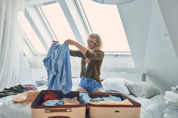 Attraktiv ung kvinna packning bagage när du sitter i sängen hemma — Stockfoto