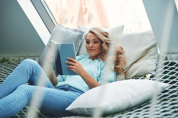Mooie jonge vrouw lezen boek terwijl ontspannen in grote hangmat thuis — Stockfoto