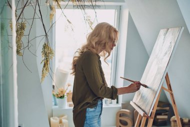 Sanat stüdyosunda resim yapan çekici genç bir kadının yan görünüşü