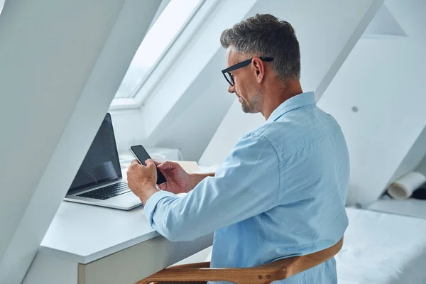 Homme mûr confiant utilisant un téléphone portable alors qu'il était assis au bureau — Photo