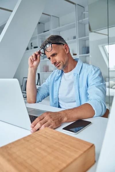 累了的成熟男人坐在写字台边的笔记本电脑上工作 — 图库照片