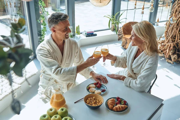 Top view of beautiful mature couple in bathrobes enjoying breakfast together while spending time in the domestic kitchen — Stock Photo, Image