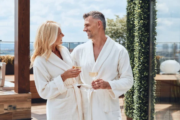 Beautiful mature couple in bathrobes enjoying champagne while relaxing in luxury hotel outdoors — Stock Photo, Image