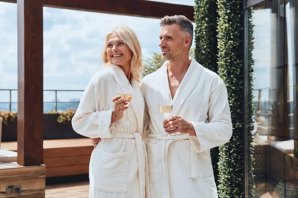 Vackra mogna par i badrockar njuter av champagne samtidigt som de kopplar av på lyxhotell utomhus — Stockfoto