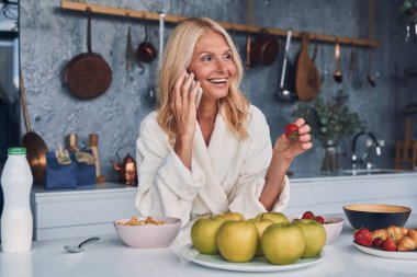 Bornozlu güzel, olgun bir kadın cep telefonuyla konuşuyor ve gülümsüyor.